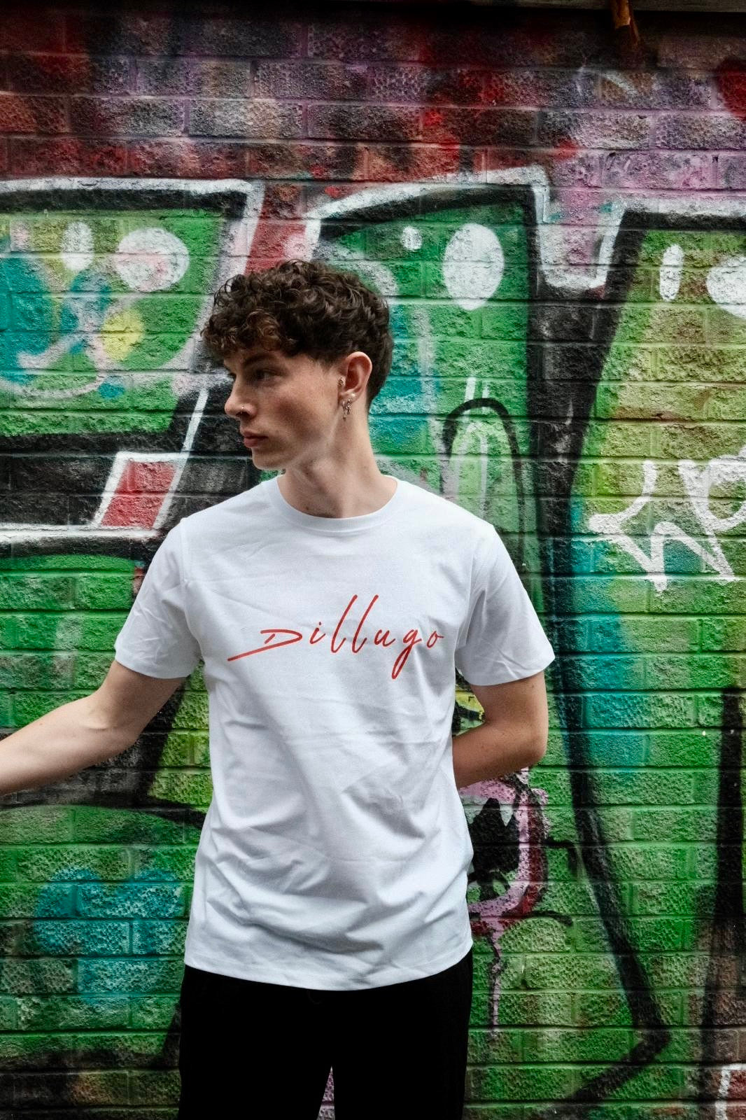 Male model looking right wearing white t-shirt with "Dillugo" written across it (in red) on a graffiti backdrop.